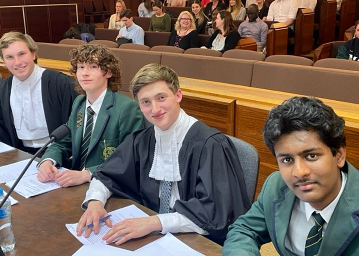 Four Mercedes College senior students in school uniform and robes preparing for a mock trial event in front of a live audience.